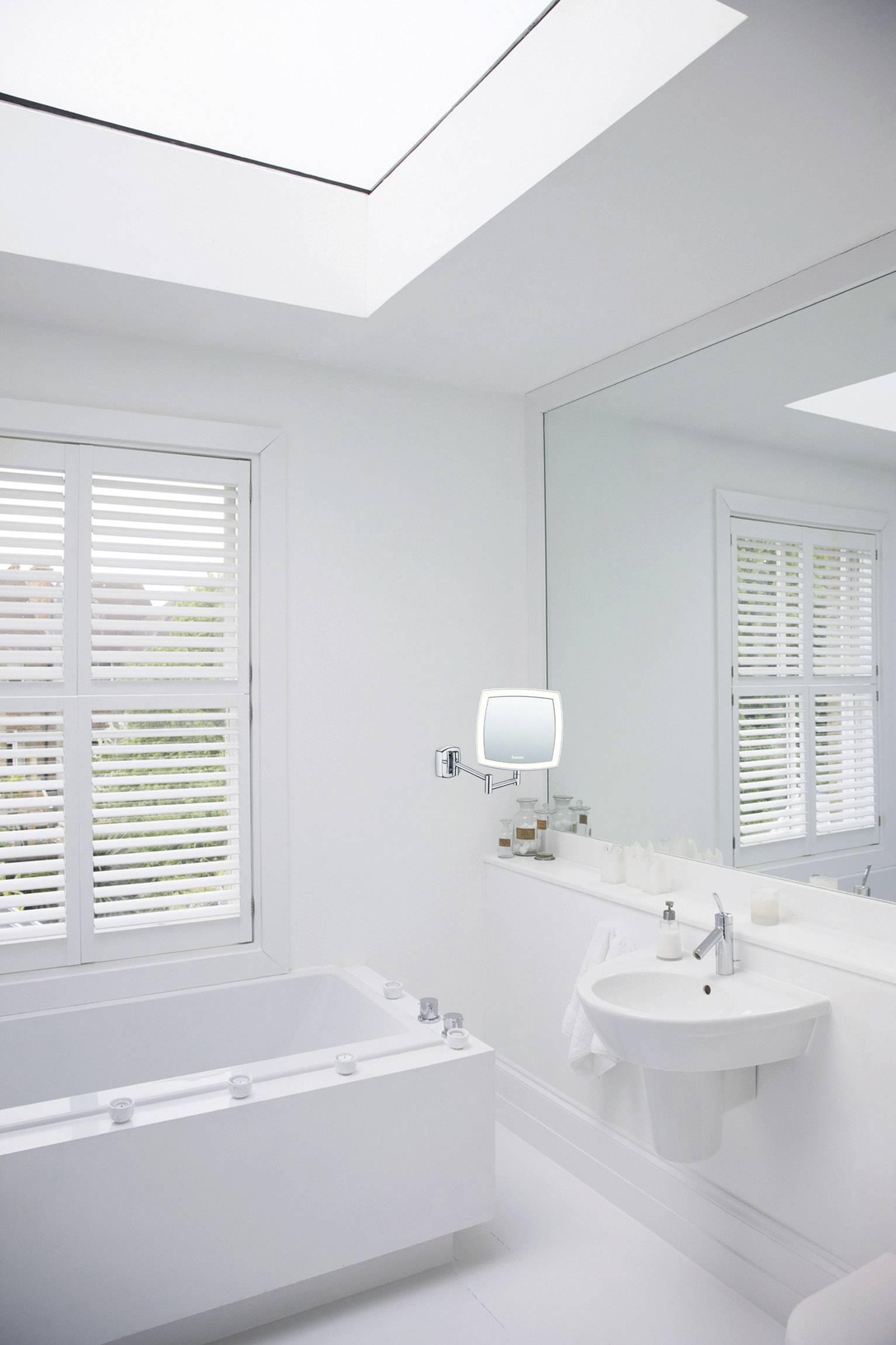 Ein modernes Badezimmer mit weißer Badewanne, großem Spiegel und Waschbecken. Helles Tageslicht strömt durch ein Oberlichtfenster.