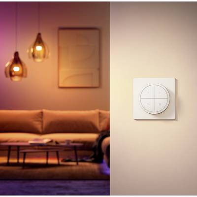 Ein stilvoller Raum mit einem modernen Sofa und Hängelampen im Hintergrund. Im Vordergrund eine innovative, quadratische Fernbedienung an der Wand.