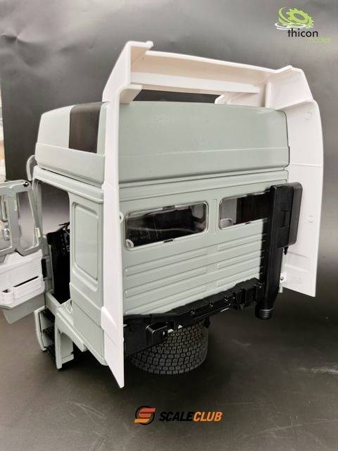 Ein Modell-Lkw-Fahrerhaus, unbemalt, mit geöffneten Türen und sichtbaren Details der Struktur. Markenlogo sichtbar unten.