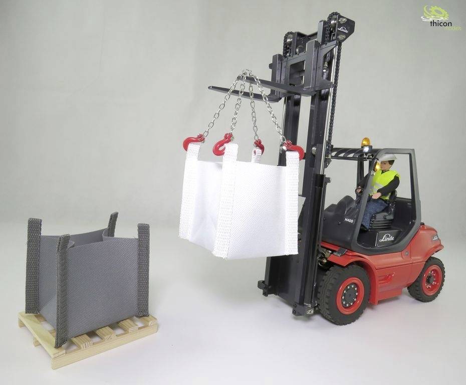 Ein Modellstapler hebt weiße, leere Bigbags mit einer Kette neben einer grauen Box auf einer Palette. Ein Arbeiter sitzt im Fahrersitz.