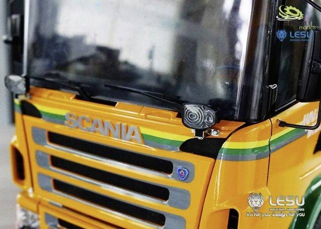 Nahaufnahme eines gelben Modell-Trucks der Marke Scania, mit farbigen Streifen und Logos an der Vorderseite.