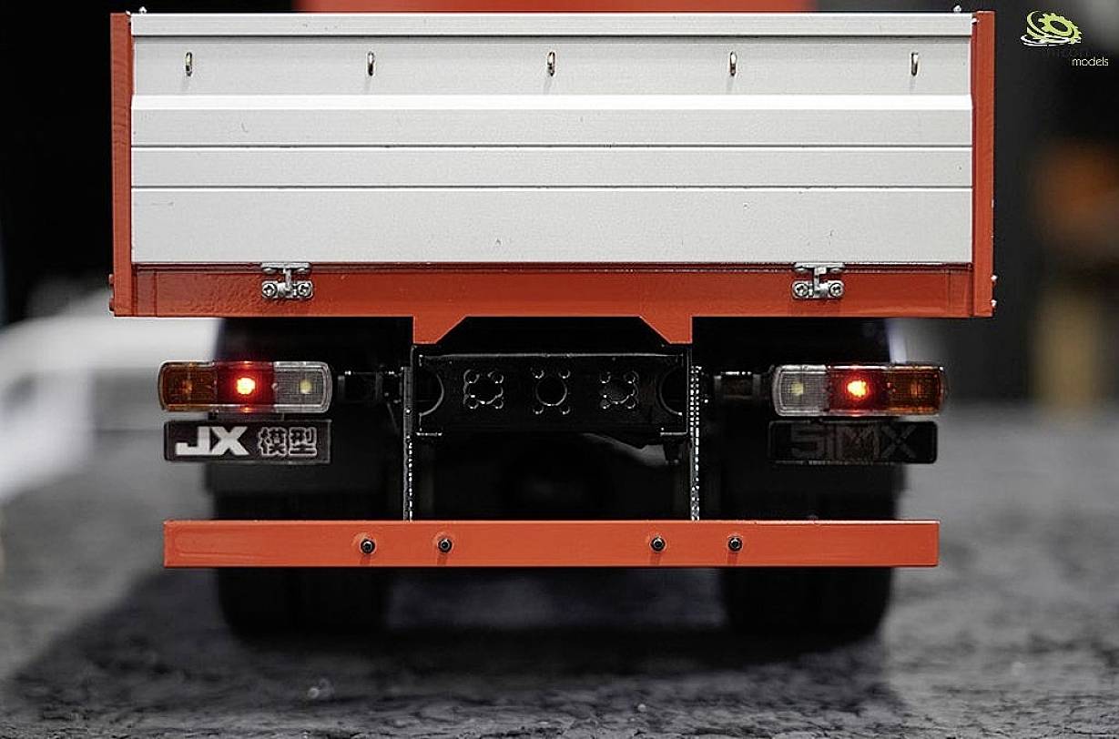 Rückansicht eines Modell-Lkw mit rotem Chassis und Metallladung. Rücklichter sind eingeschaltet. Der Fokus liegt auf Details des Modells.