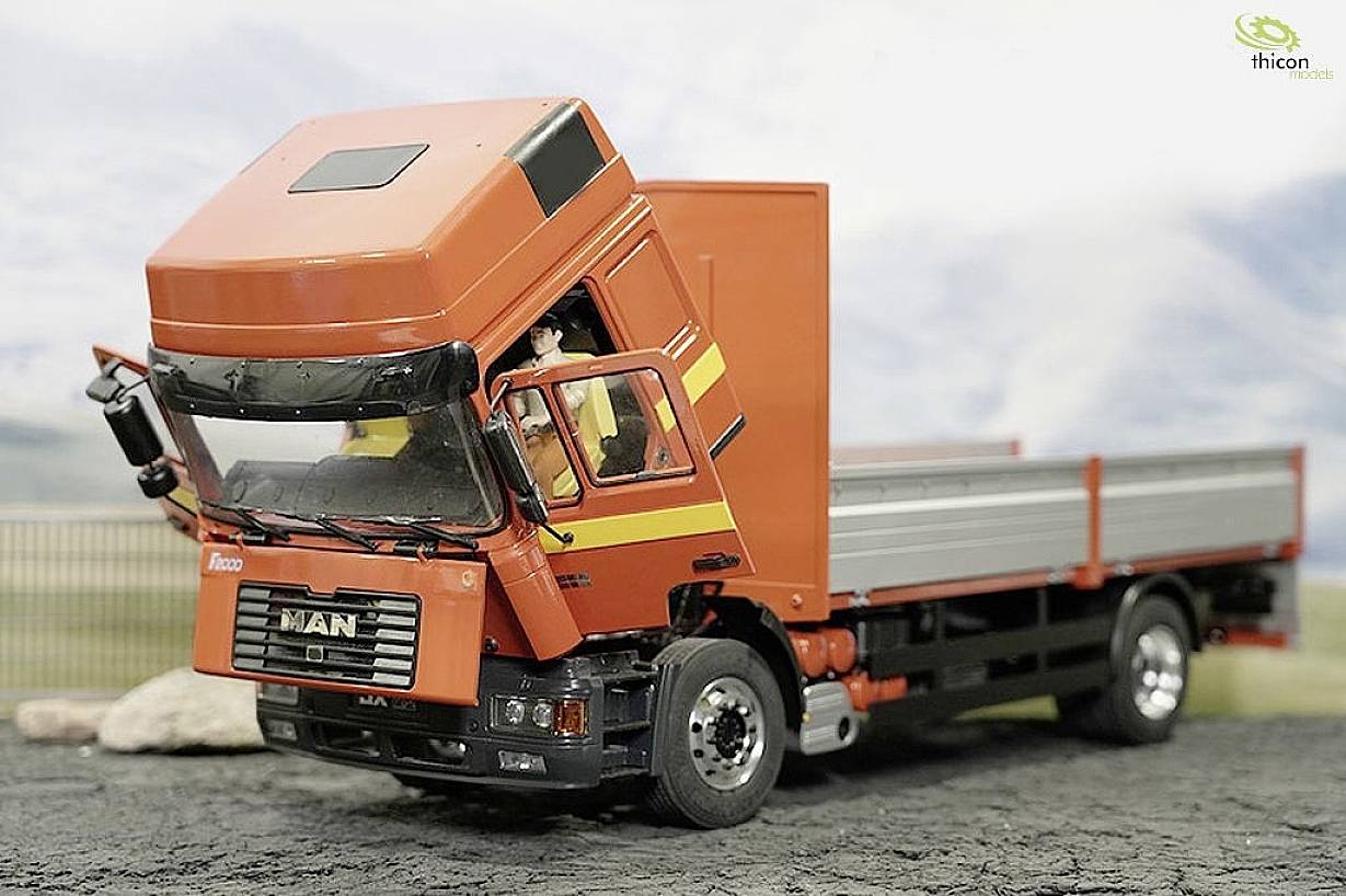 Ein rotes Modell eines Lastwagens mit geöffnetem Fahrerhaus steht auf einer grauen Fläche. Es zeigt Details des Fahrzeugs.