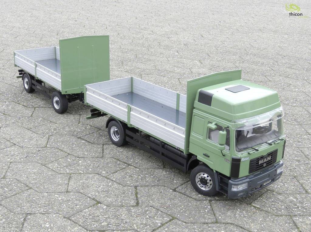 Ein grüner Modell-Lkw mit Anhänger steht auf einer gepflasterten Fläche. Der Anhänger ist offen und leer.
