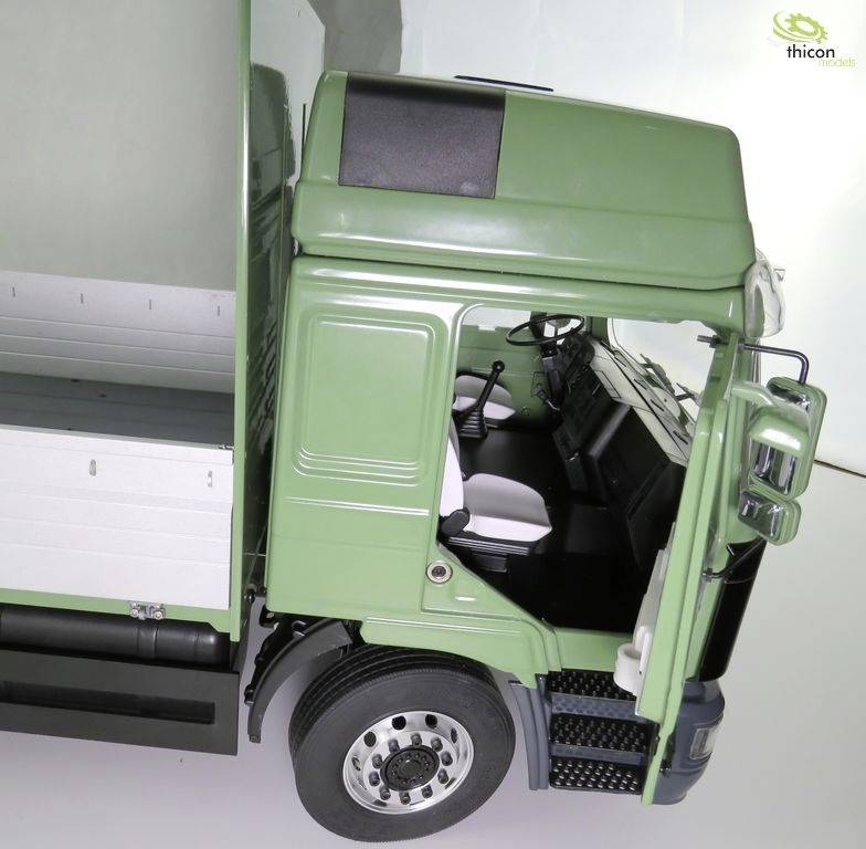 Grüner Lastwagen von oben fotografiert mit offenem Fahrerhaus, das den Fahrersitz und das Armaturenbrett zeigt. Im Hintergrund ist ein Logo sichtbar.