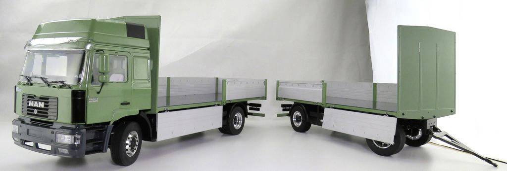 Ein grüner LKW mit Anhänger; ideal für den Transport von Gütern. Beide Teile haben offene Ladeflächen und sind für große Lasten geeignet.