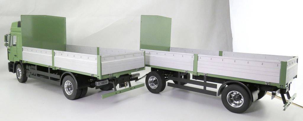 Ein Modell eines grünen Lkw mit Anhänger, beide mit weißen Seitengittern, auf einer weißen Oberfläche präsentiert.