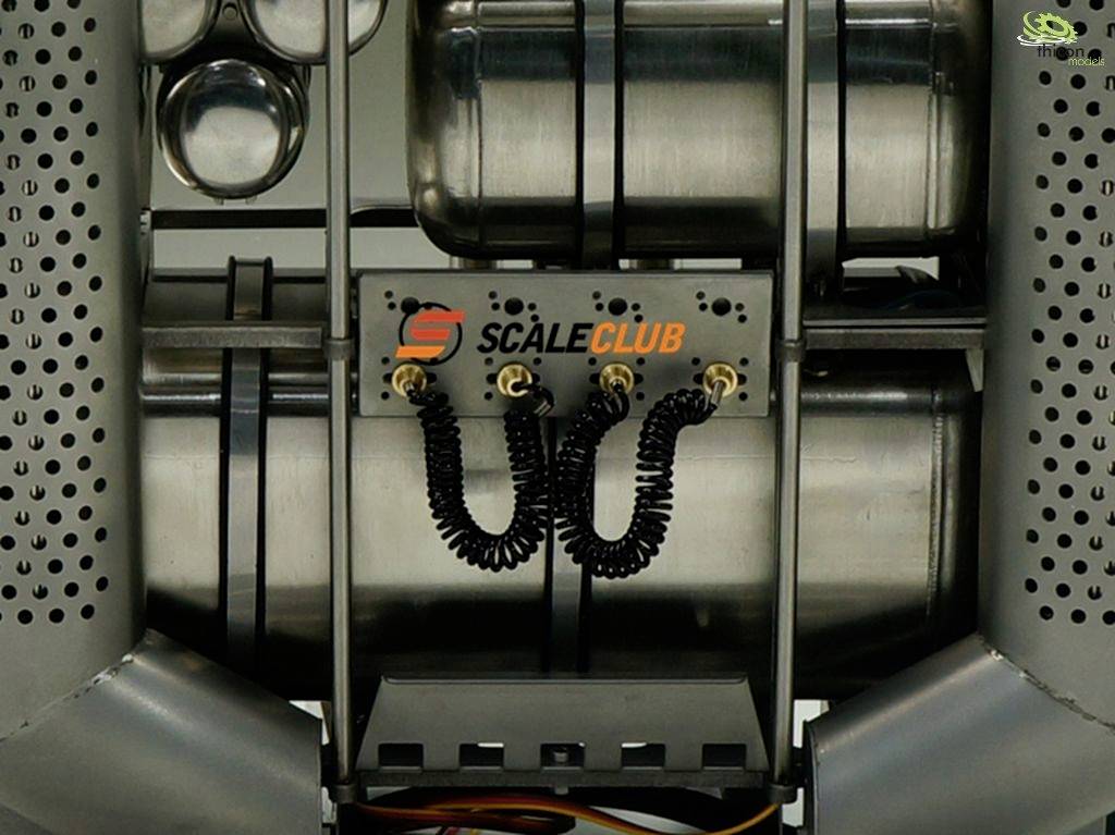 Metallisches Konstrukt mit Logo 'Scale Club', zeigt Schläuche und Metallzylinder, möglicherweise Teil einer größeren Maschine oder Apparatur.