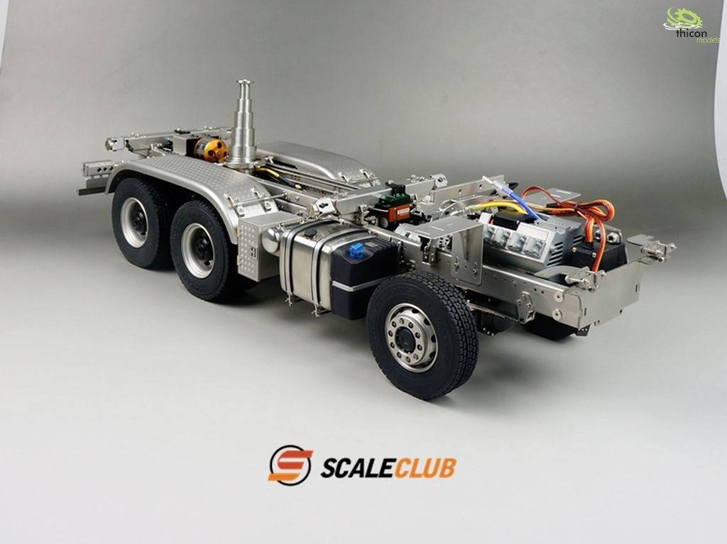 Modell eines LKW-Chassis mit sichtbar detaillierten Metallkomponenten, Verkabelung und Kleinteilen, vor grauem Hintergrund.