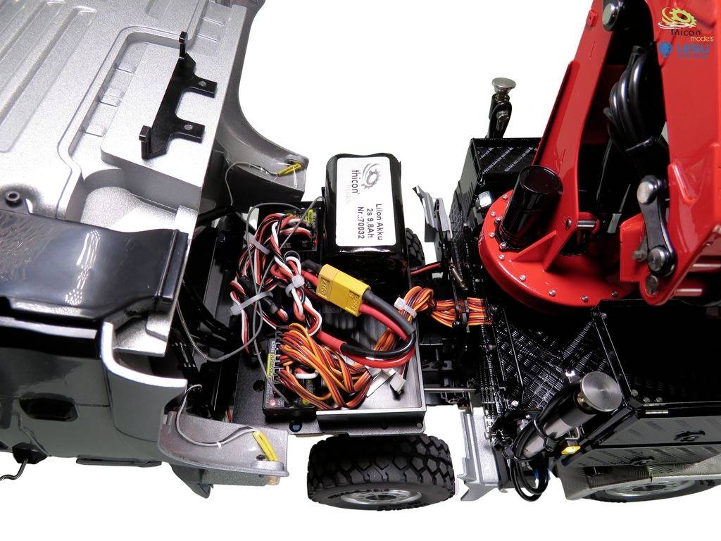 Ein geöffnetes Modellauto zeigt detaillierte Verkabelung und Elektronik im Inneren. Rechts ein rotes mechanisches Bauelement.