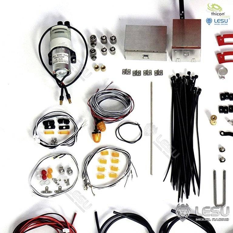 Verschiedene elektronische und mechanische Bauteile verteilt auf einer Oberfläche, darunter Kabel, Schalter und Gehäuse, für Modellbauprojekte.