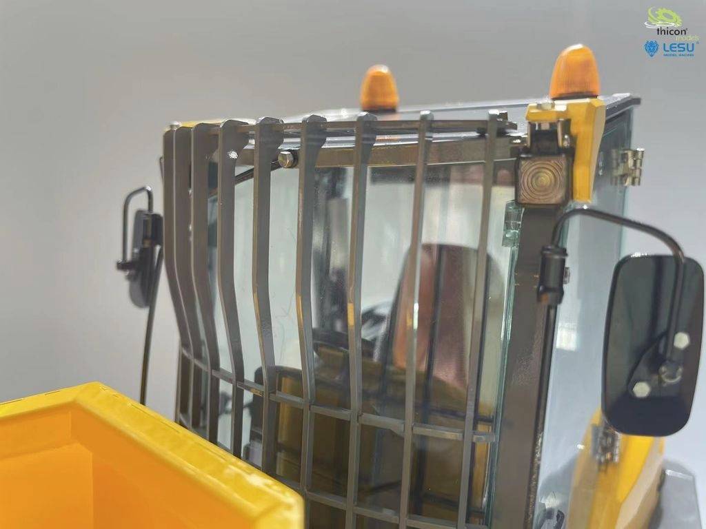 Ein gelbes Baugerät mit Schutzgitter und Warnleuchten. Es handelt sich um eine Maschinenkabine mit sichtbarer Front- und Seitenspiegeln.