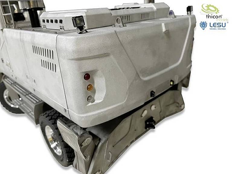 Modell eines silbernen Lastwagens von hinten, zeigt Rücklichter und Stoßstange. Im Hintergrund sind zwei Logo-Embleme zu sehen.