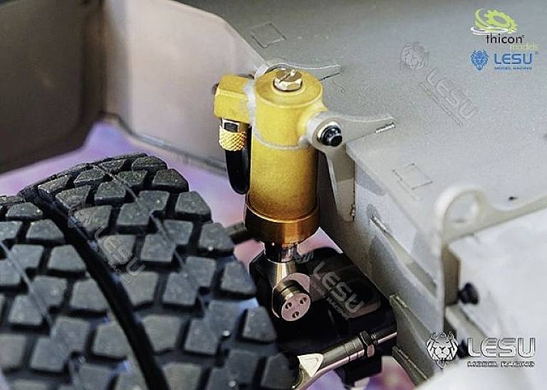 Nahaufnahme eines mechanischen Rads mit Gummireifen an einem Modellfahrzeug. Ein goldener Hydraulikzylinder ist oben befestigt.