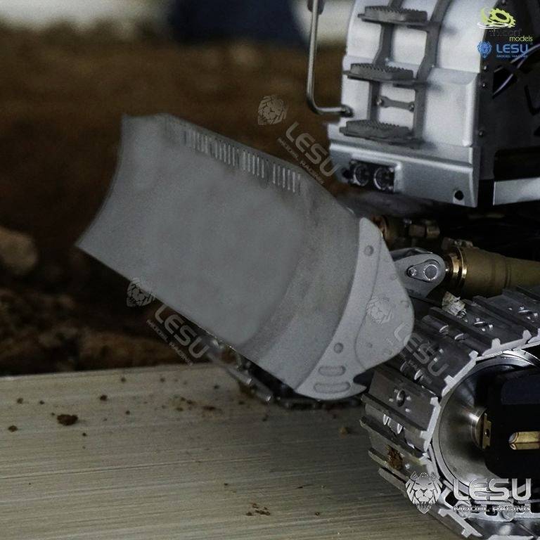 Ein Modell eines Bulldozers mit Schaufel in Bewegung, umgeben von Erde. Im Hintergrund sind unscharfe Details erkennbar.