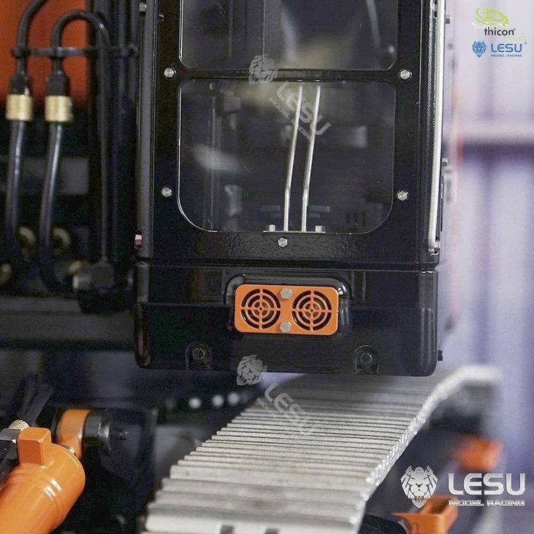 Ein schwarzes technisches Gerät mit Lüftung und Kabeln ist auf einem Metallrahmen montiert. Oben rechts sind Markenlogos sichtbar.