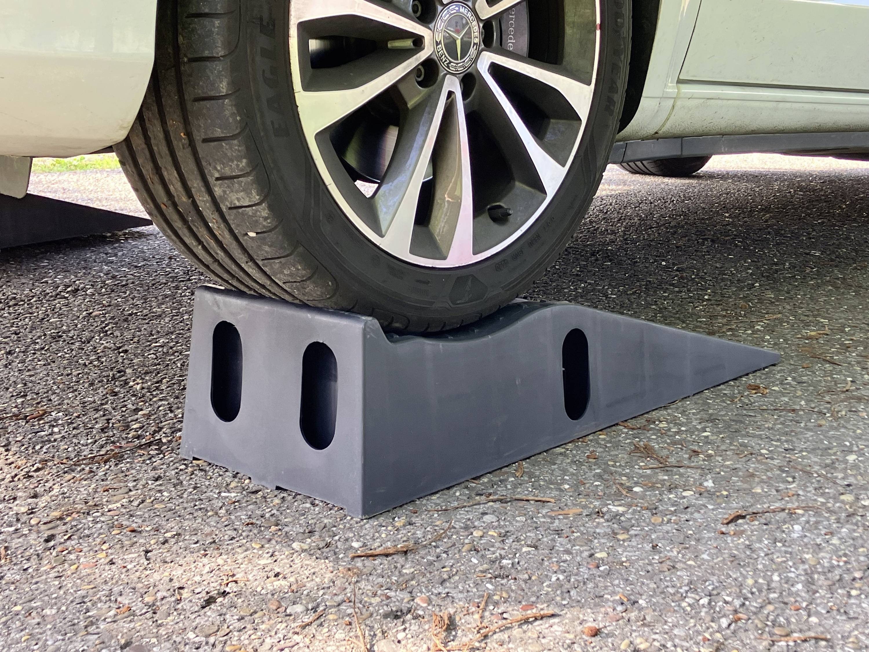 Ein Autoreifen steht auf einem schwarzen Keil, der als Auffahrhilfe dient. Der Keil hebt das Fahrzeug einseitig an.