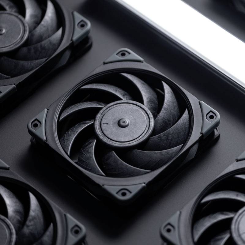 'Vier schwarze Computerlüfter mit geschwungenen Rotorblättern liegen auf einer grauen Oberfläche. Ein heller Streifen oben rechts.'