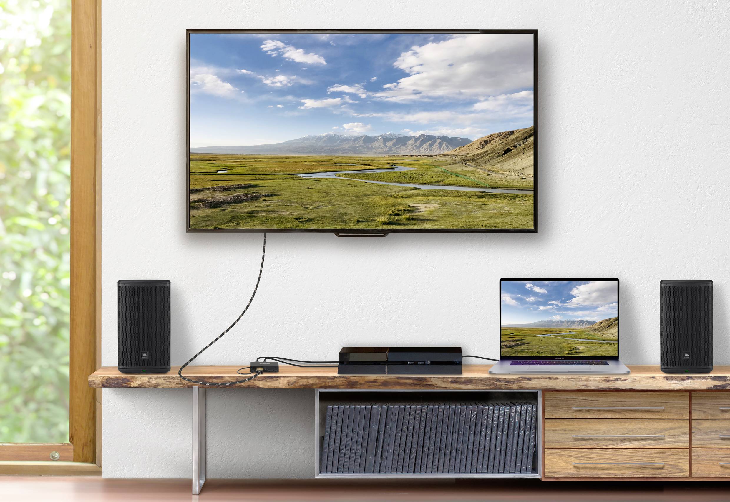 Ein Fernseher an einer Wand zeigt eine Naturlandschaft. Darunter ein Laptop mit gleichem Bild, verbunden mit einem Mediaplayer auf einem Regal.