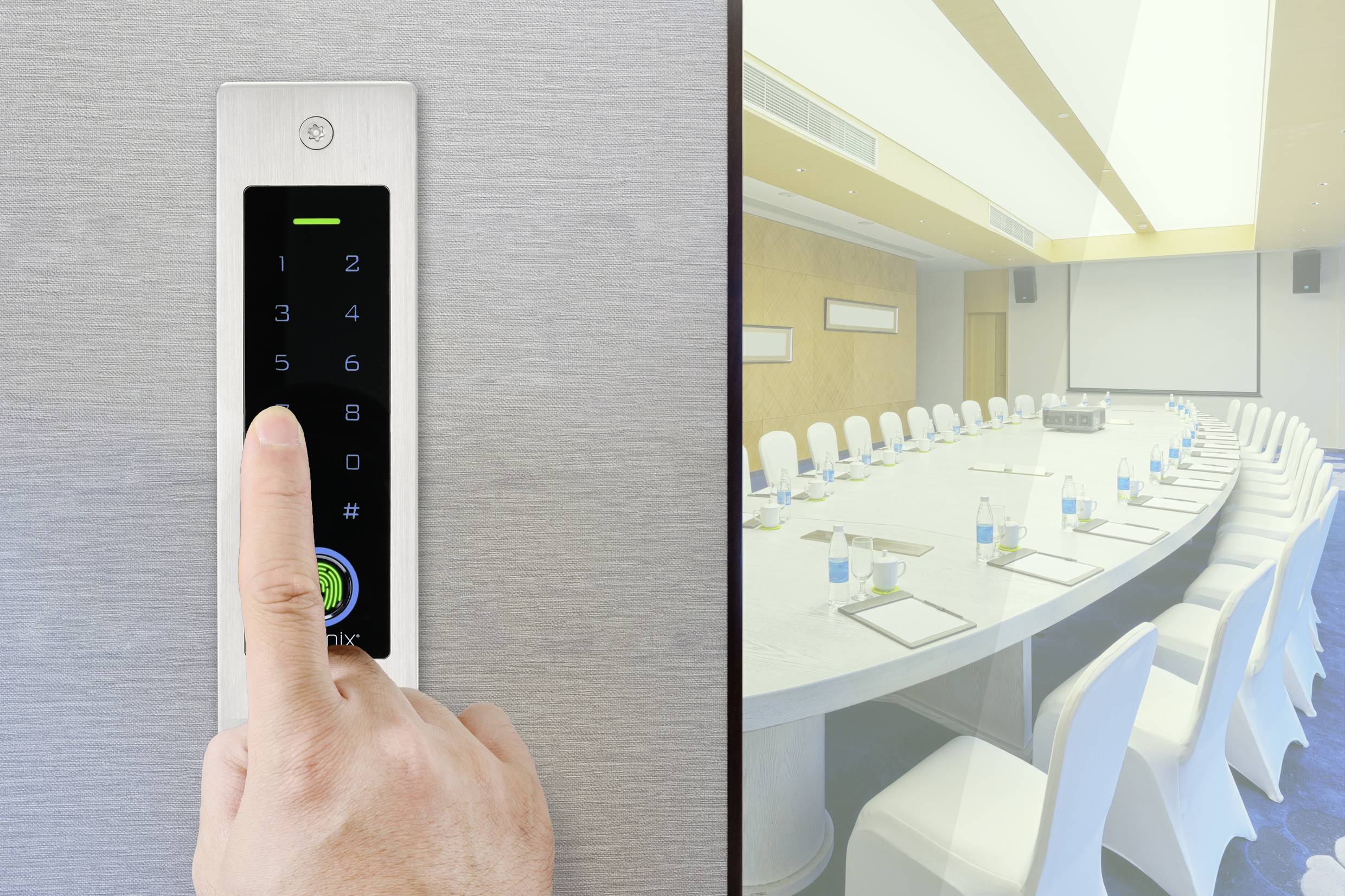 Eine Hand drückt eine Taste auf einem schwarzen Touchpad neben einem Konferenzraum mit ovalem Tisch und weißen Stühlen.