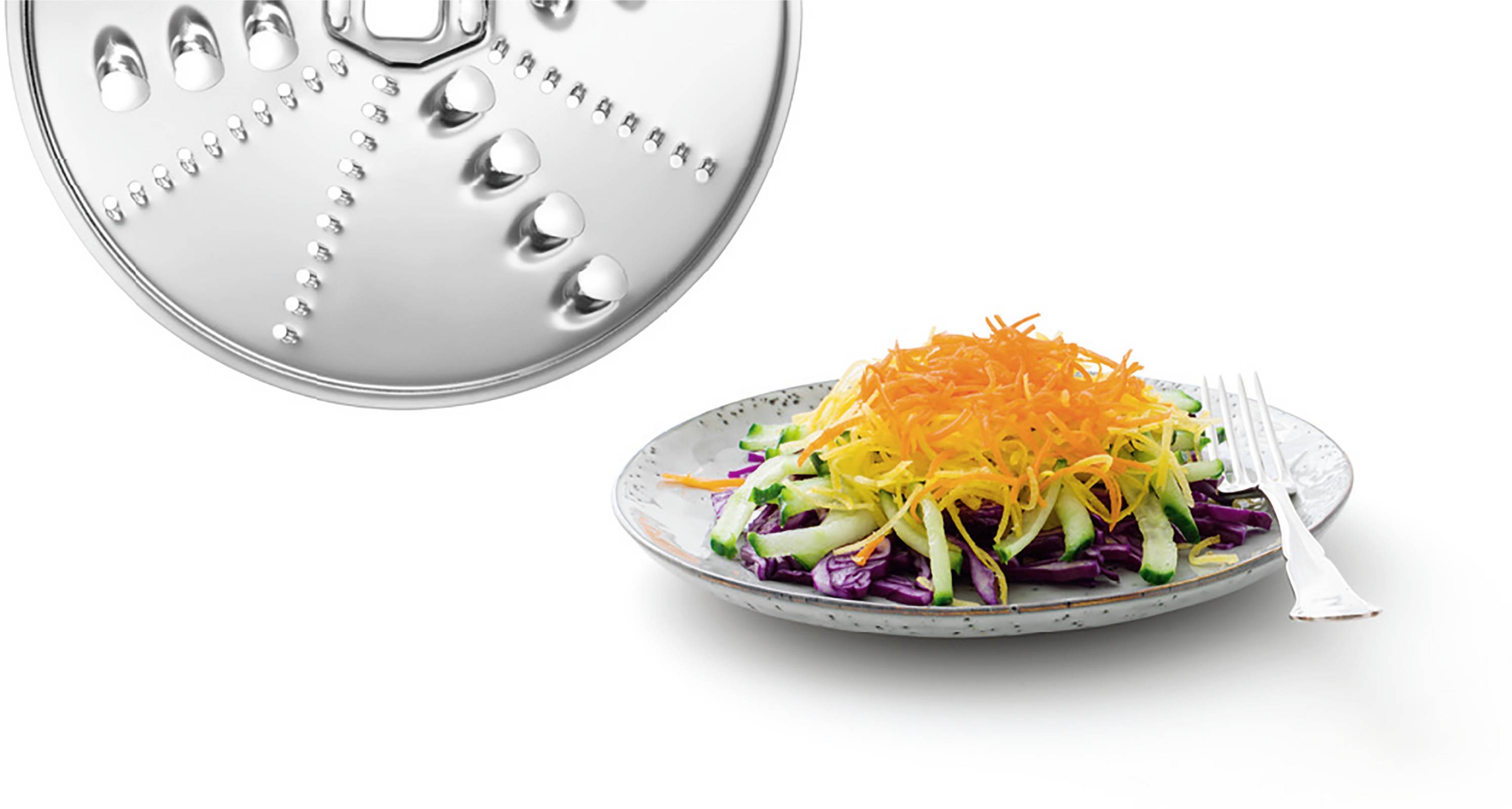 Ein Teller mit einem frischen Salat aus roten, grünen und gelben Gemüsestreifen. Daneben ist ein silbernes Küchengerät zu sehen.