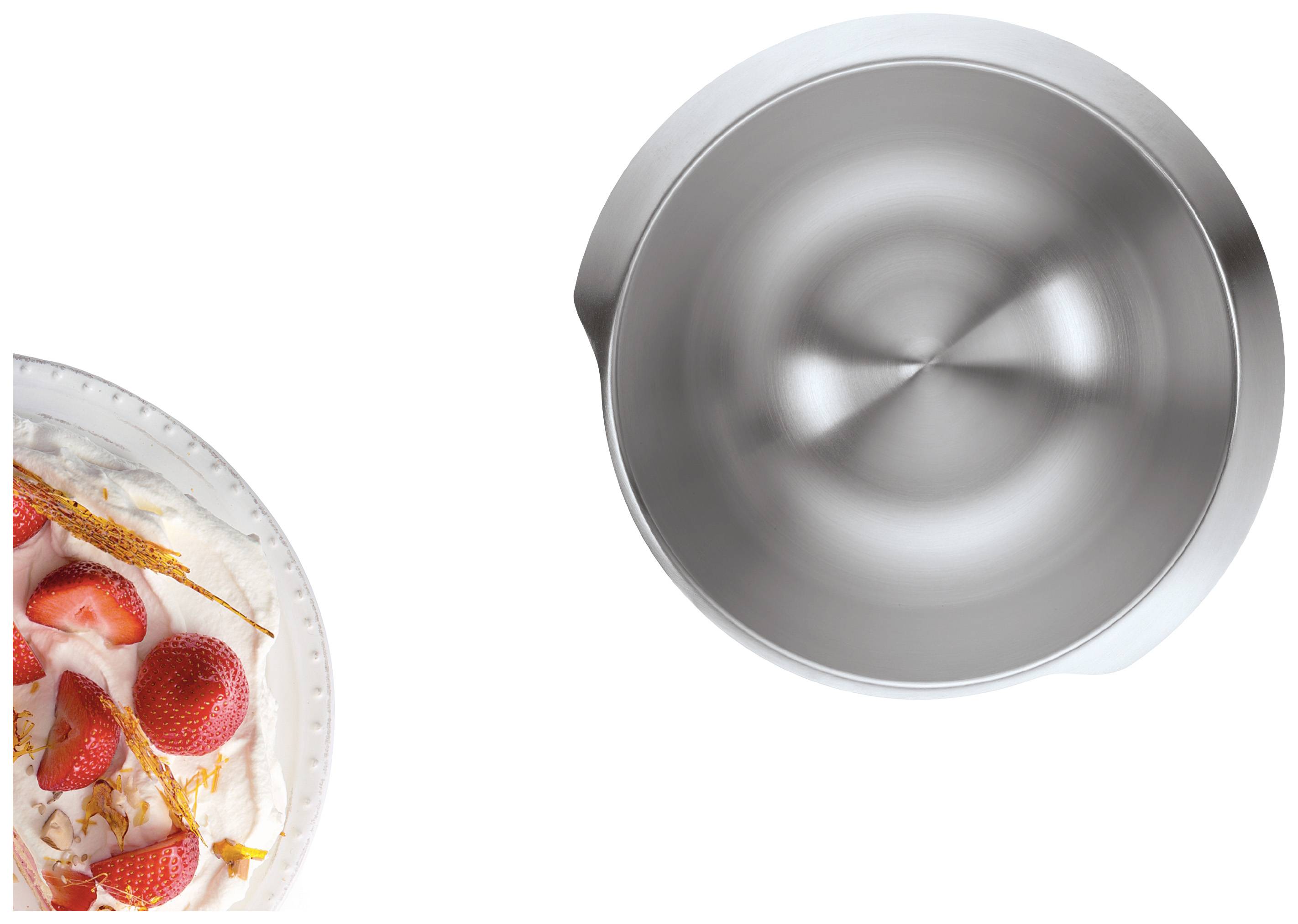 Eine Sahnetorte mit Erdbeeren links, daneben eine leere, glänzende Metallschüssel von oben gesehen.