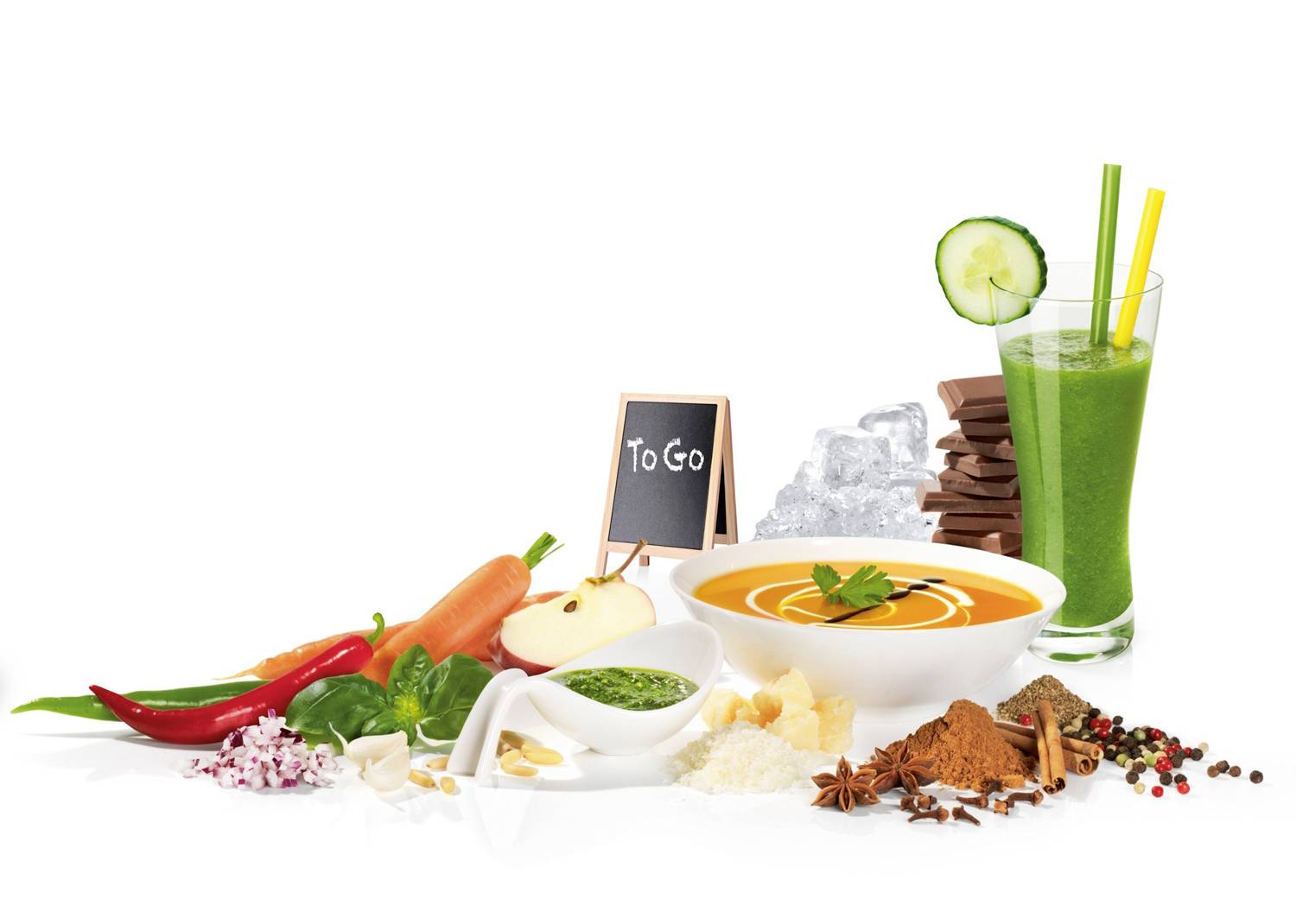 Ein Arrangement aus Gemüsesuppe, frischem Gemüse, Schokolade und grünem Smoothie auf weißem Hintergrund, mit einem 'To Go'-Schild.
