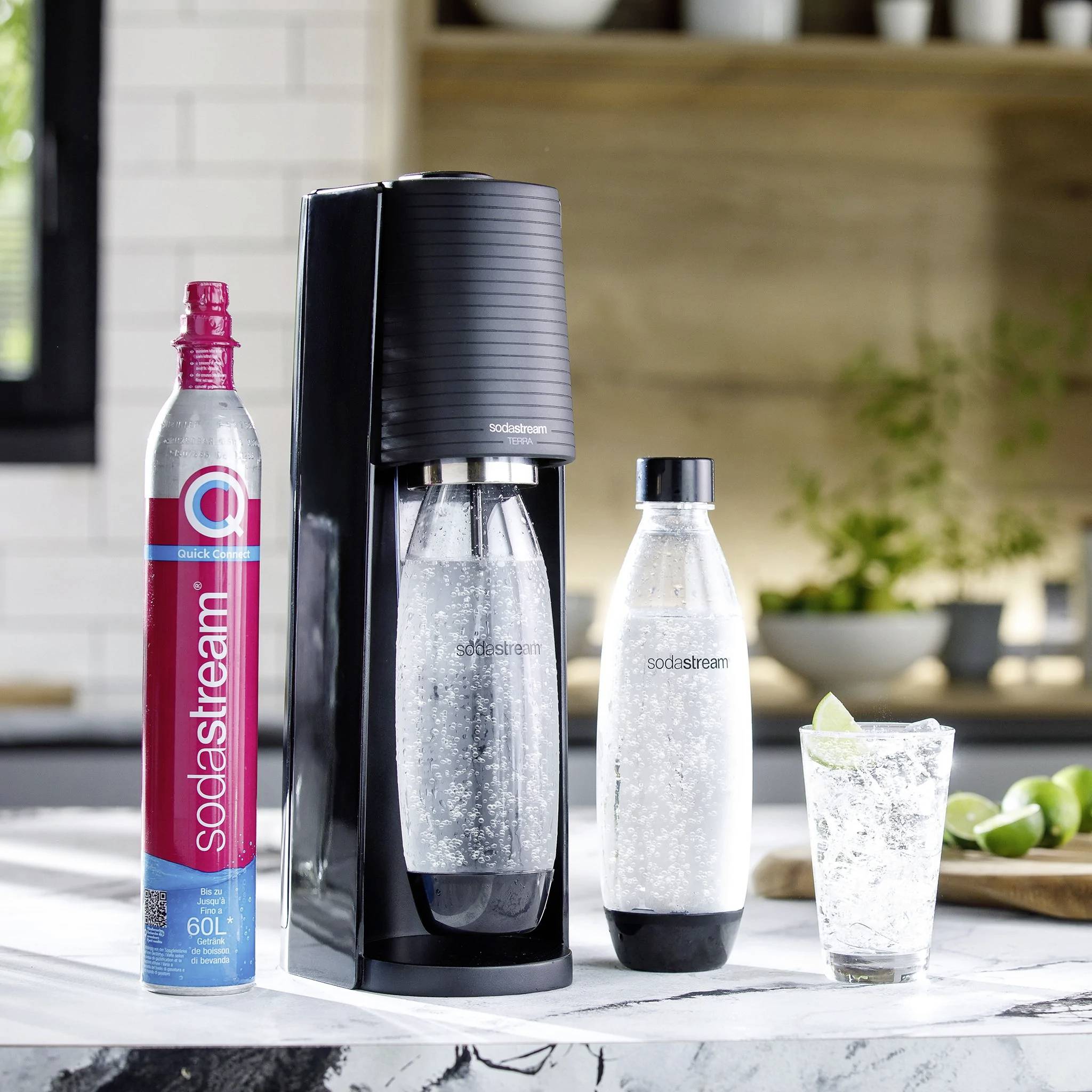 SodaStream-Gerät mit zwei Flaschen auf einer Küchenarbeitsplatte; links eine CO2-Zylinderflasche. Fertiges Sprudelwasser im Glas.