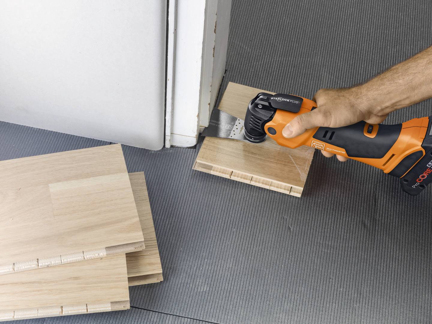 Eine Person schneidet mit einem elektrischen Multifunktionswerkzeug Holzstücke, um den Bodenbelag an eine Türöffnung anzupassen.