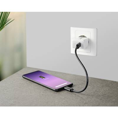 Smartphone auf einem Tisch, verbunden mit einer Steckdose über ein Ladekabel. Der Bildschirm zeigt ein Batterie-Symbol und lädt.