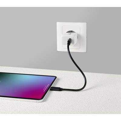 Ein Smartphone liegt auf dem Tisch und wird über ein schwarzes Kabel an einer Wandsteckdose geladen.
