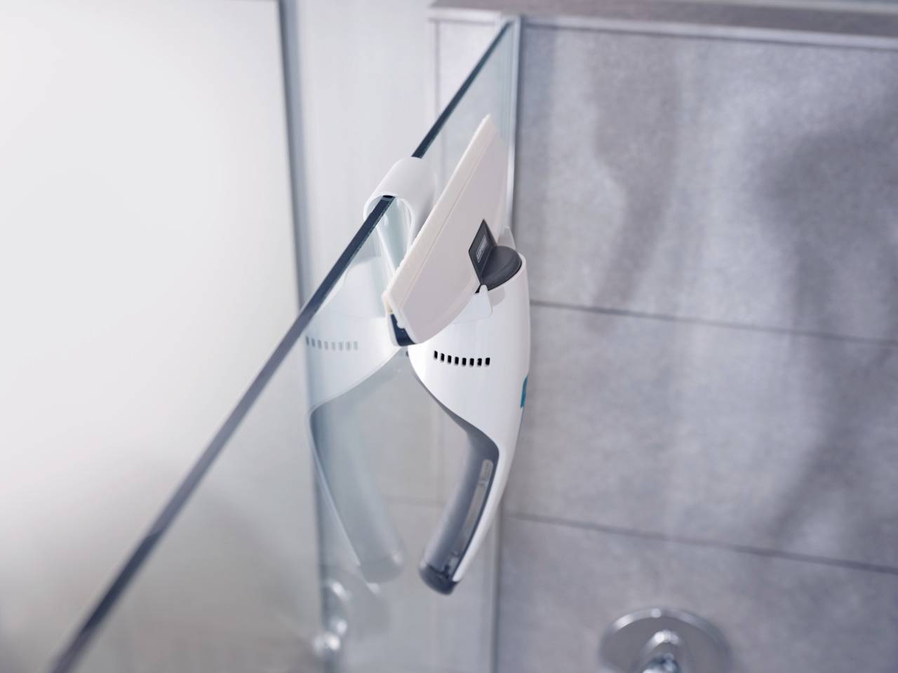 Ein weißer, batteriebetriebener Fensterreiniger reinigt vertikales Glas in einem Badezimmer.