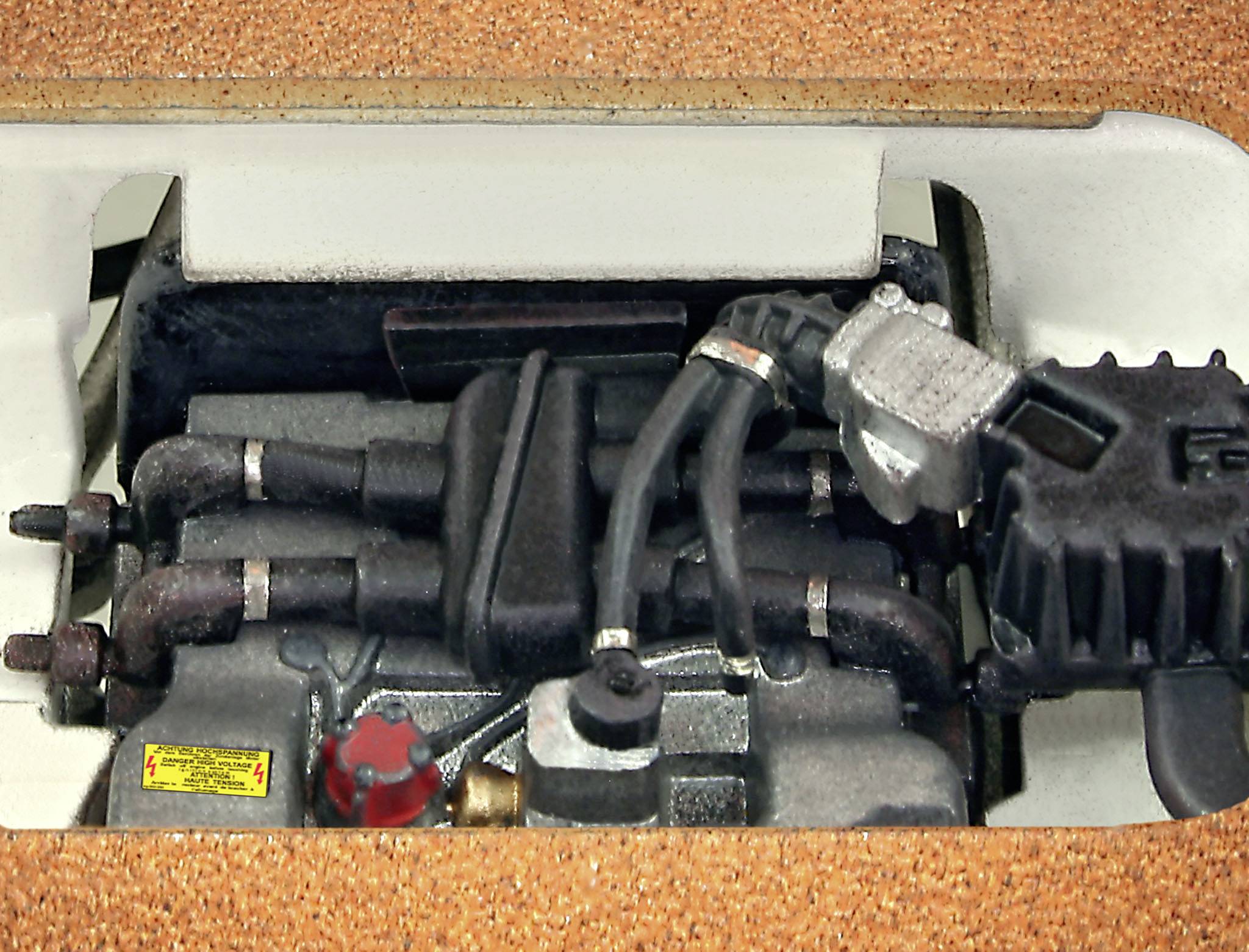 Ein Motor mit mehreren Schläuchen und Kabeln, eingebaut in einem Fahrzeug oder Gerät, von oben gesehen.