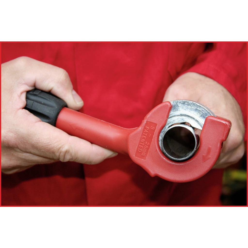 Ein rotes Rohrschneidewerkzeug in der Hand eines Menschen wird verwendet, um ein Metallrohr zu schneiden. Handschuhe schützen die Hände.