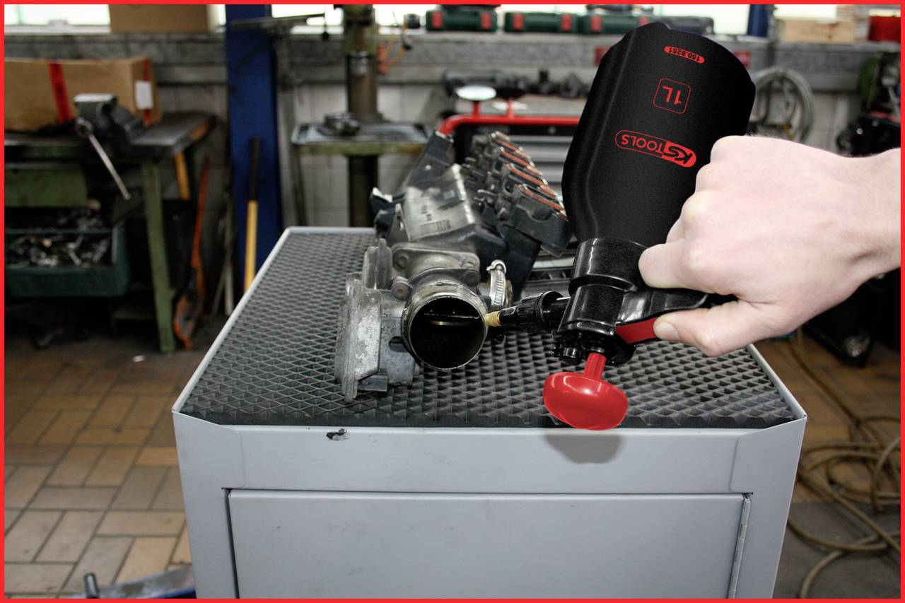 Eine Hand hält ein Werkzeug über einem Autoteil auf einem Werkstatttisch, vermutlich bei der Wartung oder Reparatur des Teils.