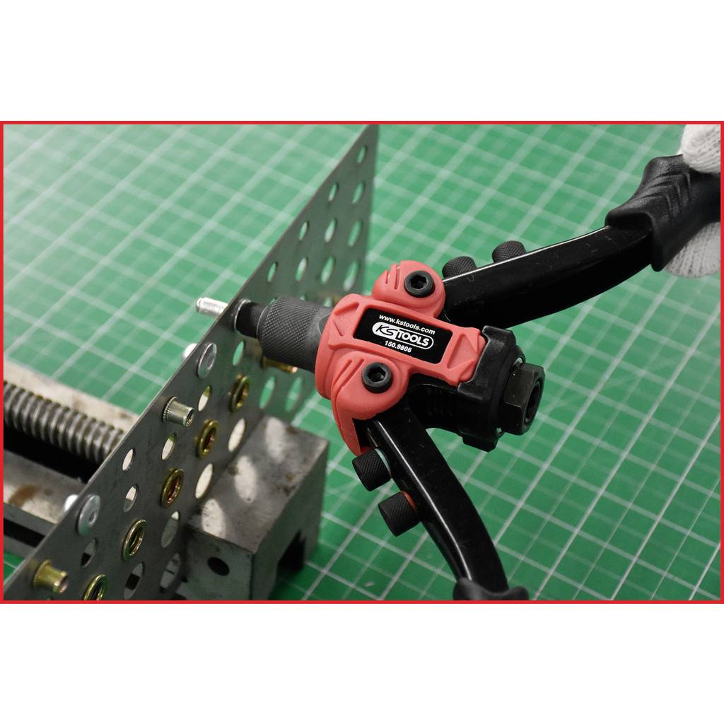 Eine rote und schwarze Nietzange wird benutzt, um eine Metallplatte mit mehreren Löchern zu bearbeiten, auf einem grünen Rasterhintergrund.