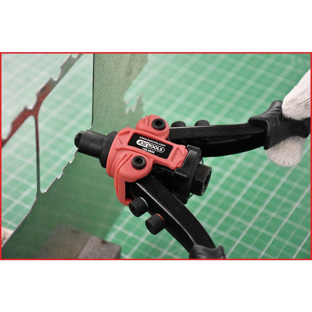 Eine rote Handwerkzeugzange schneidet ein Stück Draht auf einem grünen Hintergrund. Eine behandschuhte Hand hält die Zange.