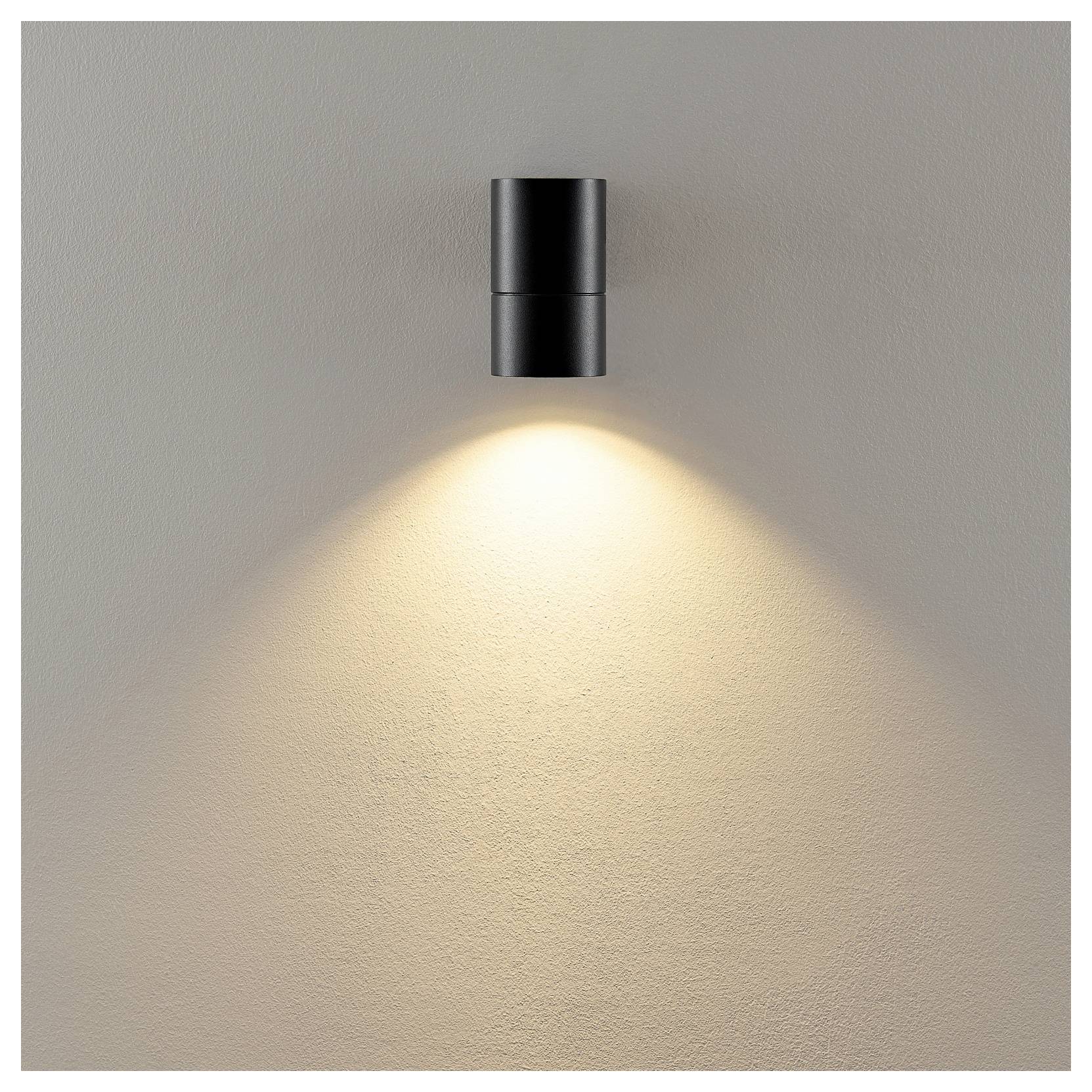 Schwarze Wandleuchte, die einen warmen Lichtkegel auf eine beige, strukturierte Wand wirft.