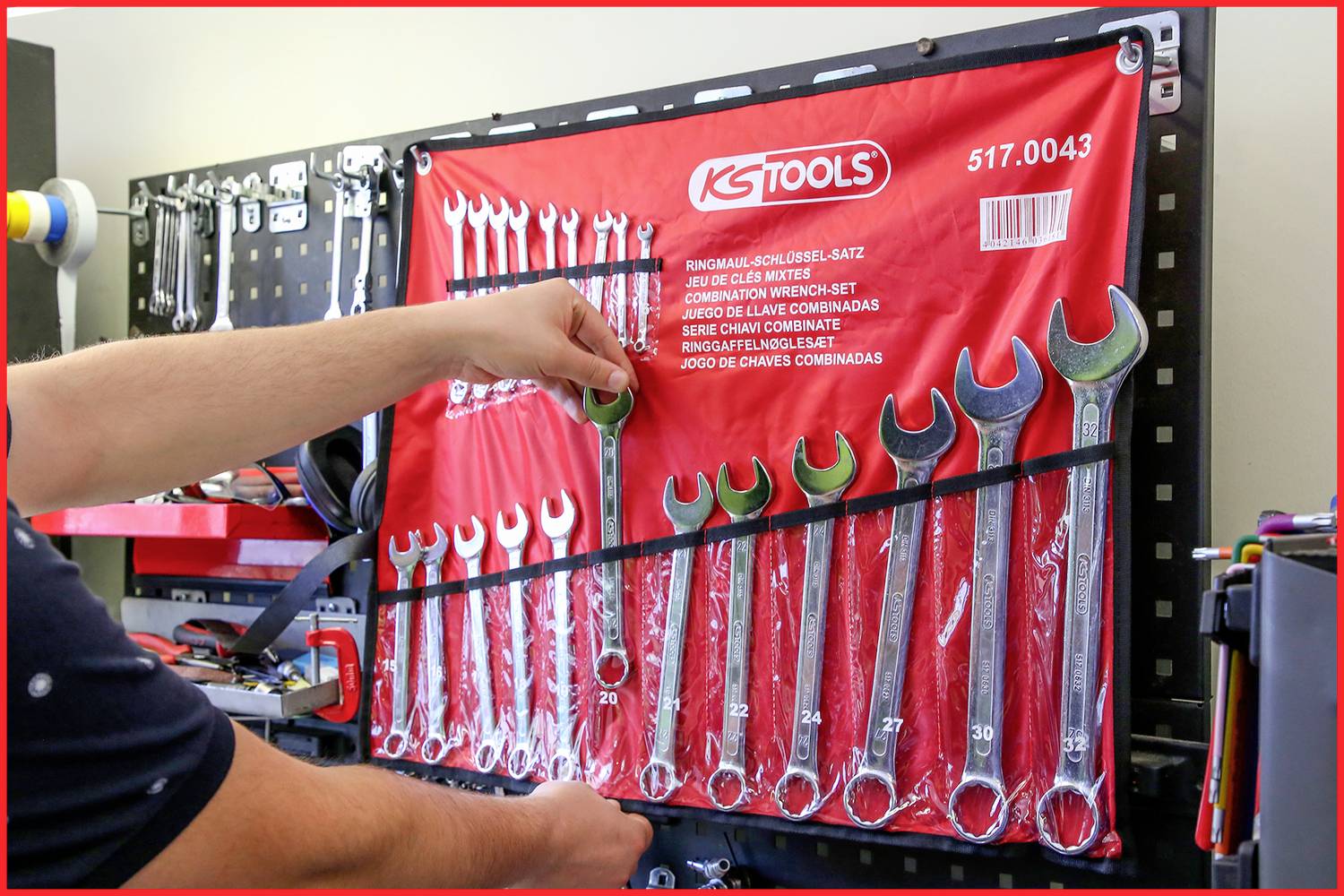 Person organisiert Maulschlüssel in einer Werkstatt. Eine rote Werkzeugtafel von KS Tools hält verschiedene Schlüsselgrößen.