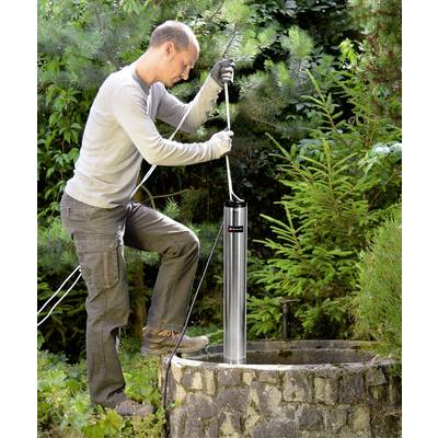 Ein Mann installiert eine Pumpe in einem Gartenbrunnen. Er trägt Arbeitshandschuhe und steht neben grünen Pflanzen.