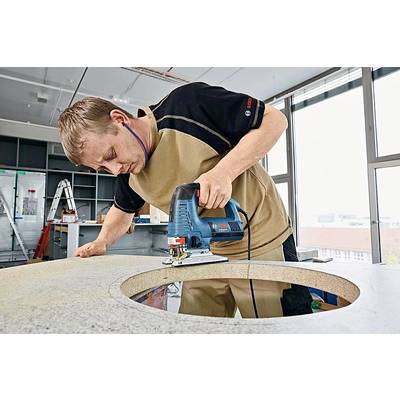 Ein Handwerker schneidet ein rundes Loch in eine Arbeitsplatte mit einer Stichsäge in einer Werkstattumgebung bei Tageslicht.