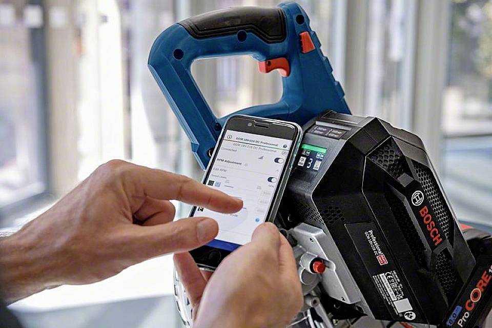Eine Hand bedient ein Smartphone, das mit einem Bosch-Elektrowerkzeug verbunden ist. Auf dem Bildschirm sind Einstellungen sichtbar.
