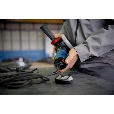 Eine Person in Arbeitskleidung hält eine blaue Elektrowerkzeug-Maschine mit Kabel, wahrscheinlich in einer Fabrikumgebung.