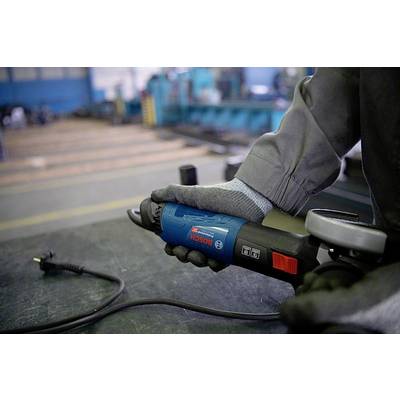 Person in grauer Arbeitskleidung hält einen blauen Winkelschleifer ohne angeschlossenes Kabel in einer Werkstatt.