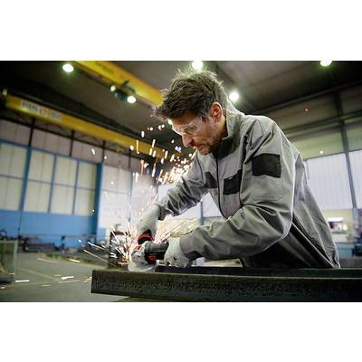 Ein Mann schleift in einer Werkhalle ein Metallstück mit einem Winkelschleifer. Funken sprühen. Er trägt Schutzbrille und Arbeitskleidung.