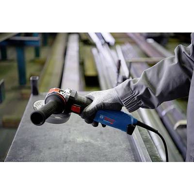 Eine Person in Arbeitskleidung hält einen Winkelschleifer über einem Metalltisch. Schutzhandschuhe sind zu sehen.