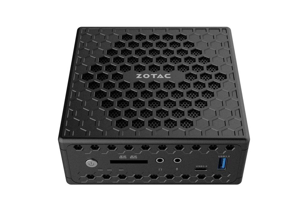 Ein kompakter, quadratischer Mini-PC in Schwarz mit Wabenmuster und dem Schriftzug 'ZOTAC' auf der Oberseite. Vorderseite mit Anschlüssen.