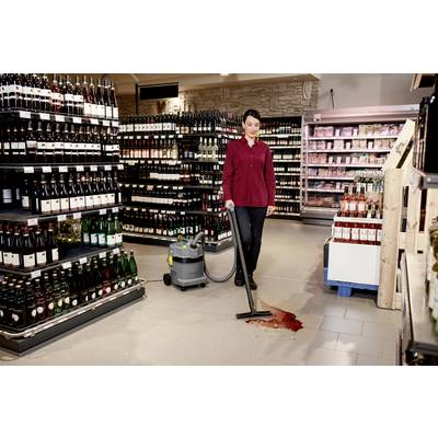 Eine Person in einem Geschäft, die eine verschüttete Flüssigkeit auf dem Boden mit einem Staubsauger reinigt, umgeben von Regalen, die mit verschiedenen Flaschen und Produkten gefüllt sind.