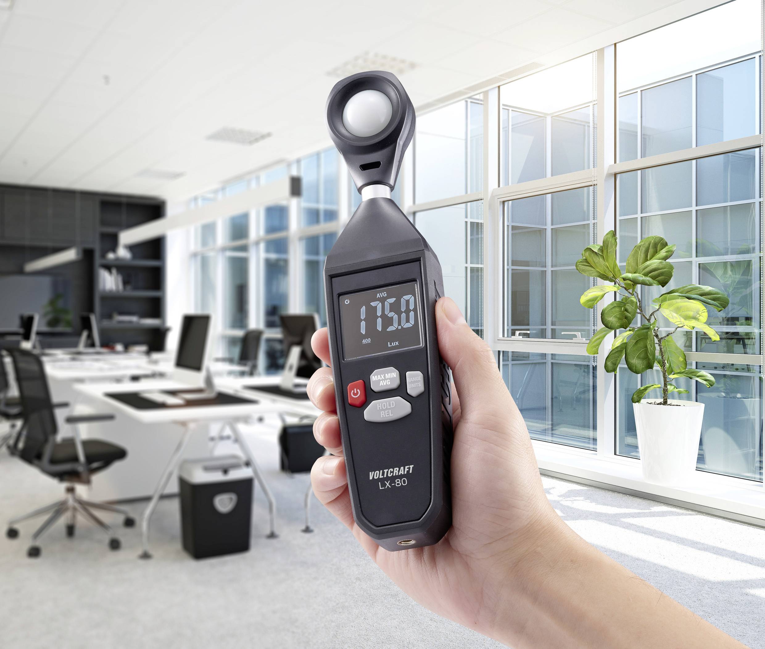 Ein Handmessgerät zeigt einen Wert von 1750 an, gehalten von einer Hand in einem modernen Büro mit großen Fenstern und Pflanzen.