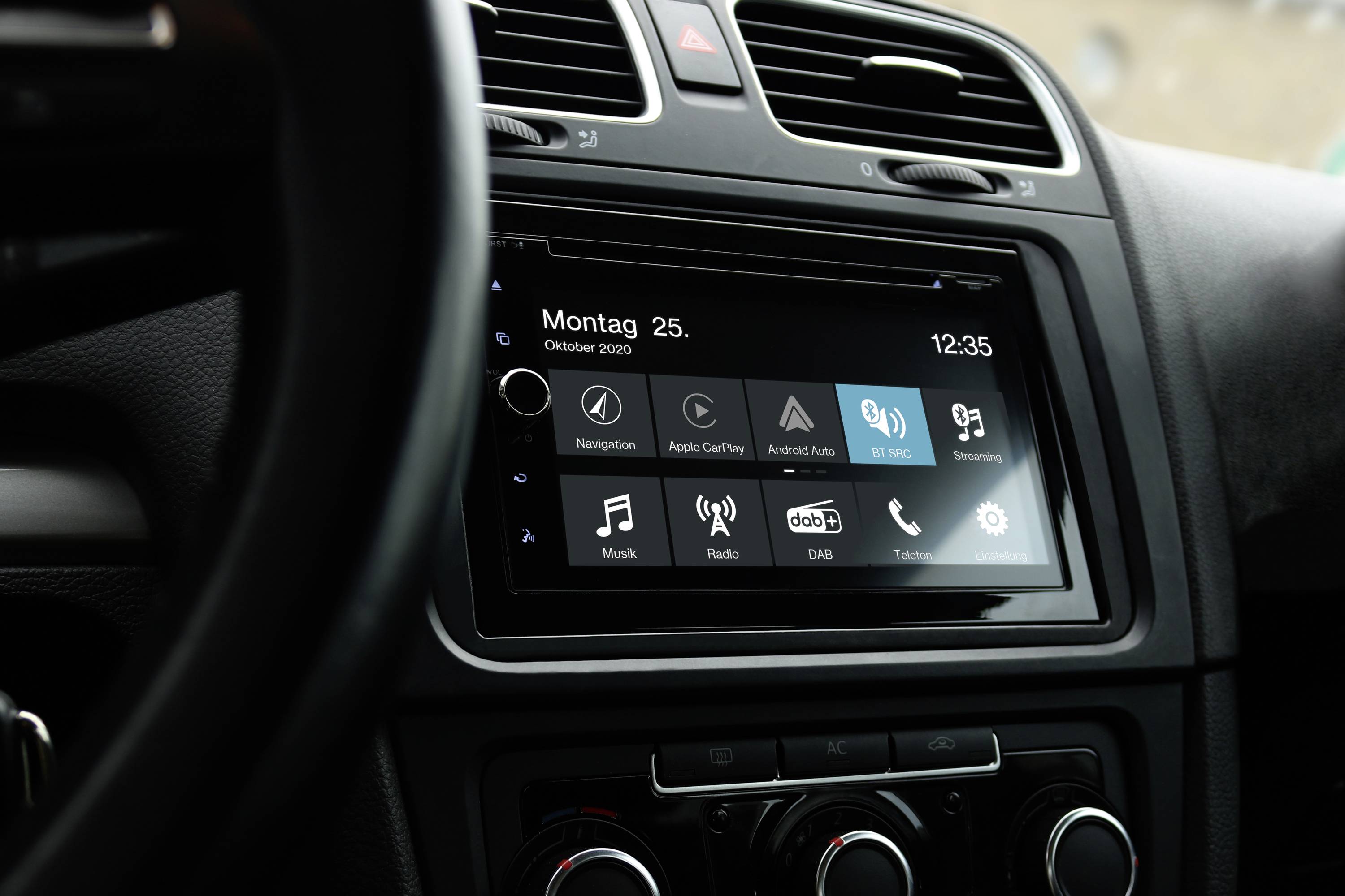 Ein Auto-Display zeigt eine Benutzeroberfläche mit Datum 'Montag, 25. Oktober 2020' und Uhrzeit '12:35', sowie Apps wie Musik und Navigation.